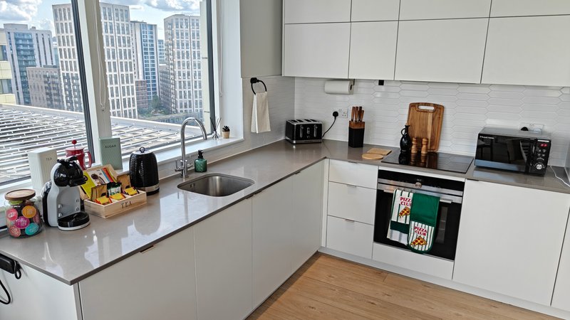Modern white kitchen with grey countertop, integrated appliances, and city skyline views through large windows