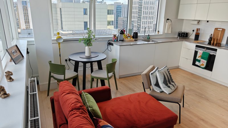 Modern open-plan living space with red sofa, dining table, kitchen area and city views