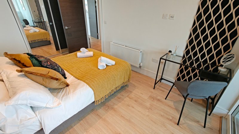 Modern bedroom with double bed, yellow throw, white pillows and black metal chairs