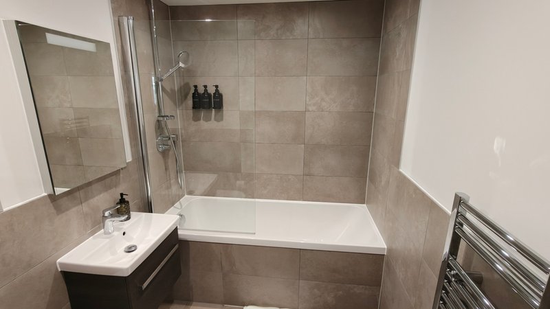 Modern bathroom with white bathtub, tiled walls, sink and mirror