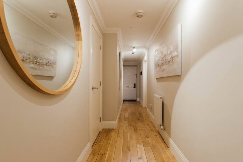 Bright hallway with wooden flooring, round mirror, framed artwork, and recessed lighting