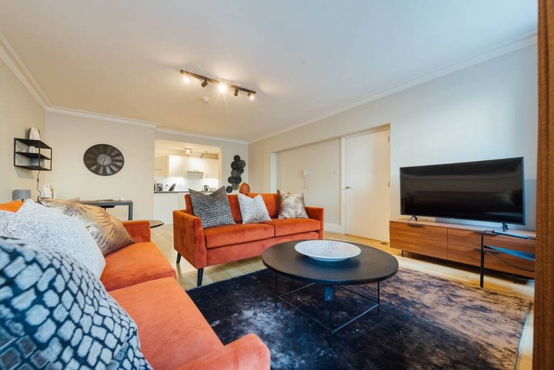 Open-plan bedroom and living area with orange sofa, TV, bed with patterned bedding, and round coffee table