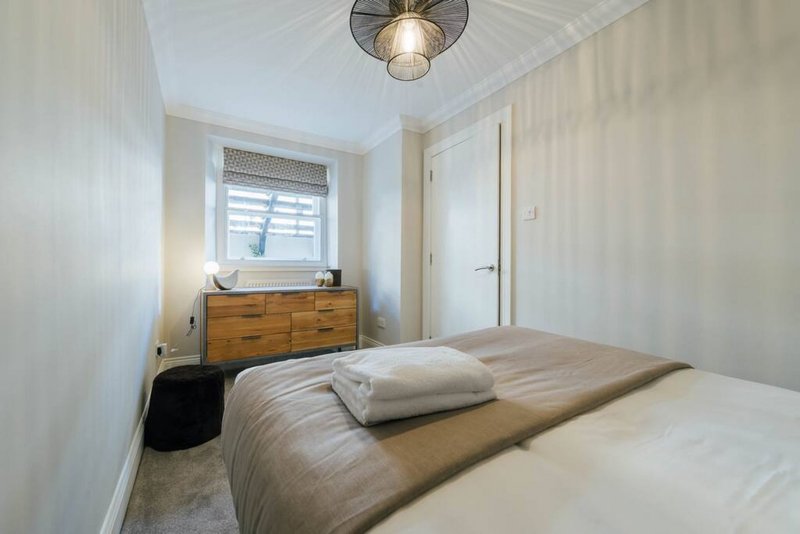 Bright bedroom with double bed, wooden dresser, ceiling lamp and window with shutters