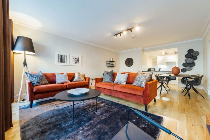 Modern living room with orange sofas, blue rug, black coffee table and open-plan kitchen