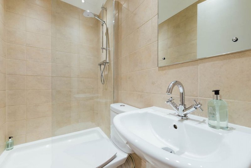 Modern bathroom with beige tile walls, white sink, mirror, shower enclosure and toilet
