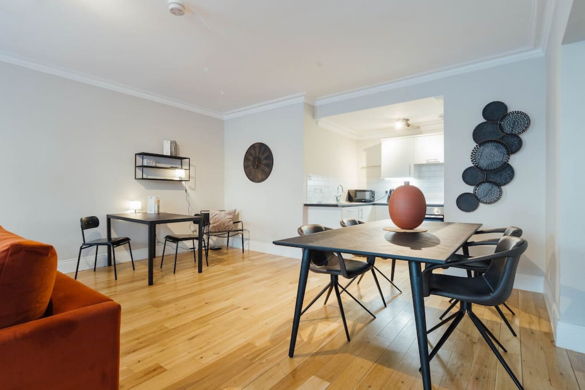 Open-plan living and dining area with wooden floors, orange sofa, black dining tables and chairs