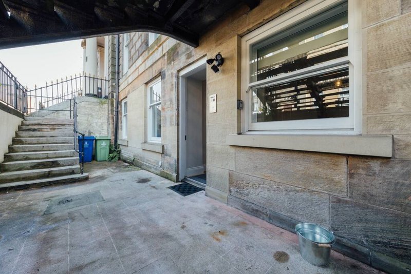 External building entrance with stone patio, grey door, window, and metal railings