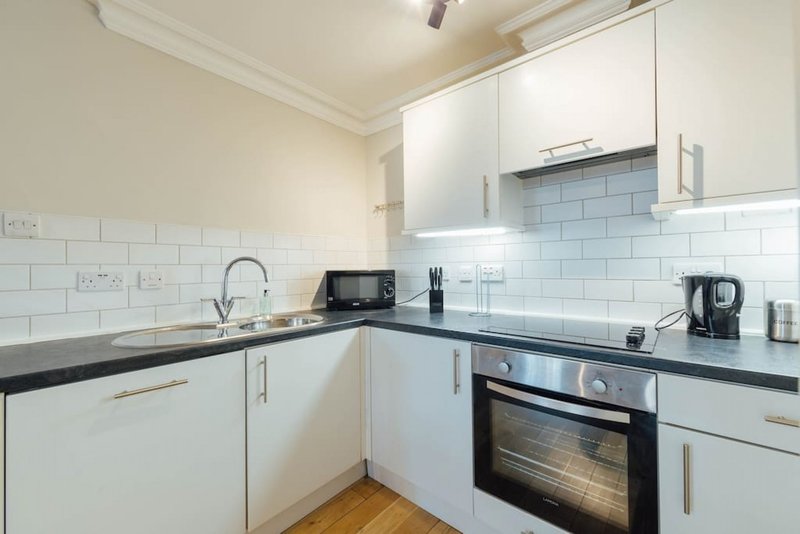 Modern white kitchen with black countertop, built-in oven, sink and electric kettle