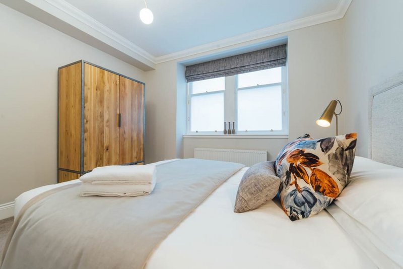 Bright bedroom with double bed, wooden wardrobe, window with blinds and bedside lamp