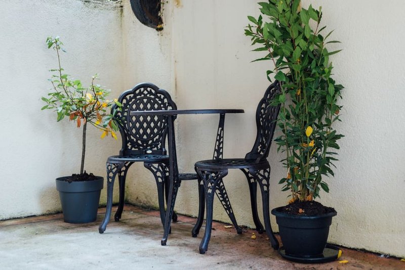 Outdoor patio area with black metal chairs, small table, and potted plants against white wall