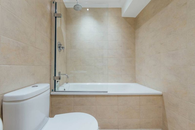 Modern bathroom with white toilet, bathtub with glass shower screen and beige tile walls