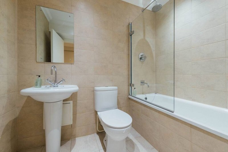 Modern bathroom with pedestal sink, toilet, bathtub with glass screen and mirror