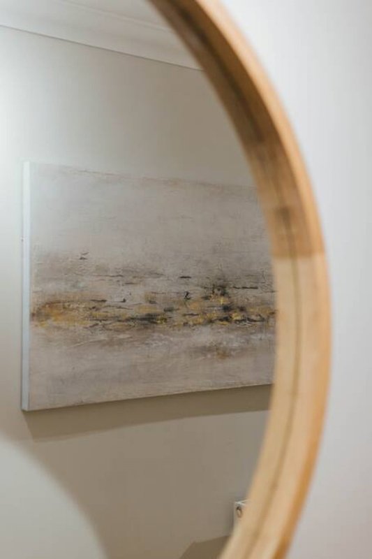 Wall-mounted abstract artwork with natural wooden-framed mirror in modern interior