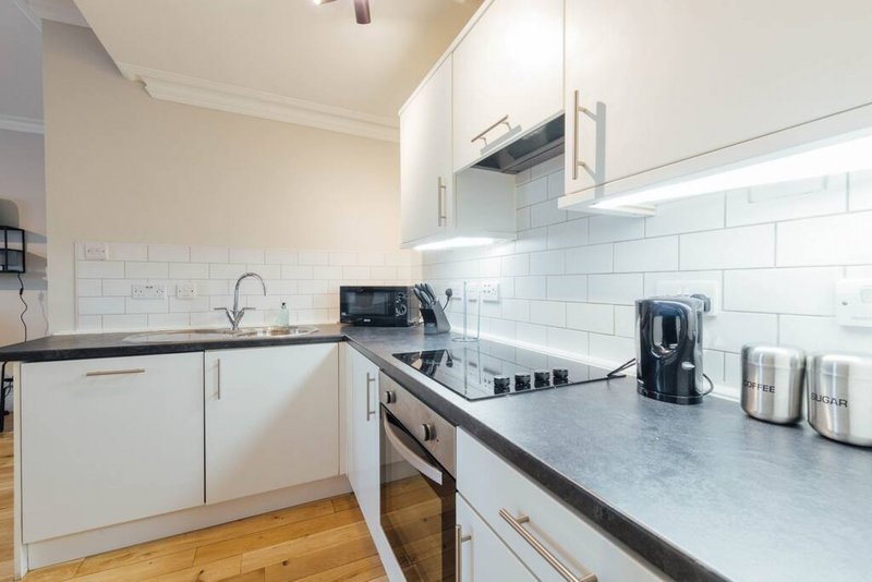 Modern kitchen with white cabinetry, stainless steel appliances, white subway tile backsplash and wooden flooring