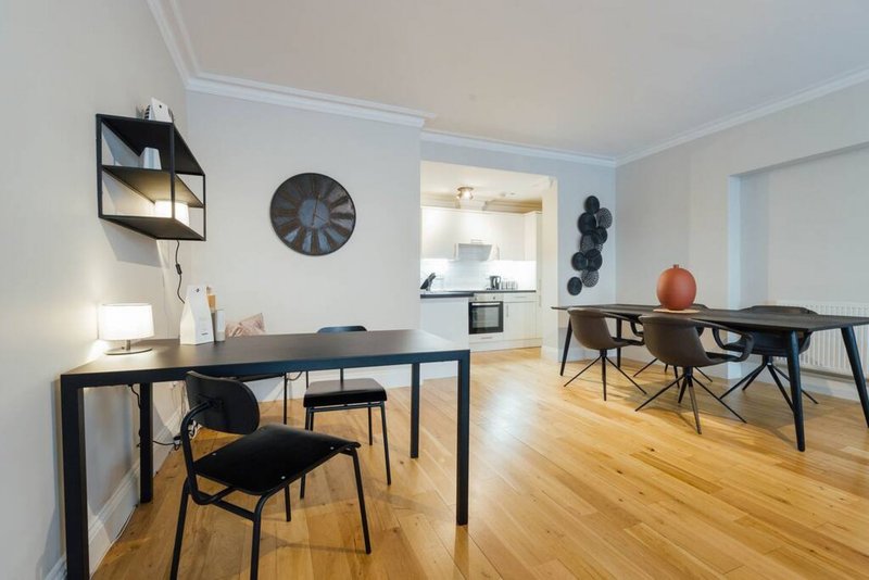 Modern open-plan workspace with two black desks, wooden flooring, wall clock and decorative items