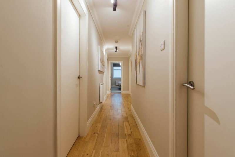 Long hallway with wooden flooring, white walls, multiple doors, and natural light