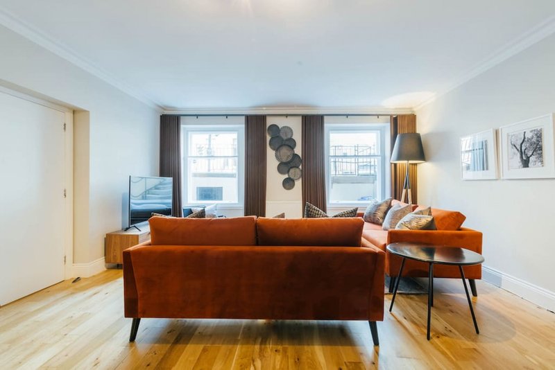 Bright living room with orange velvet sofa, wooden floor, windows and modern decor