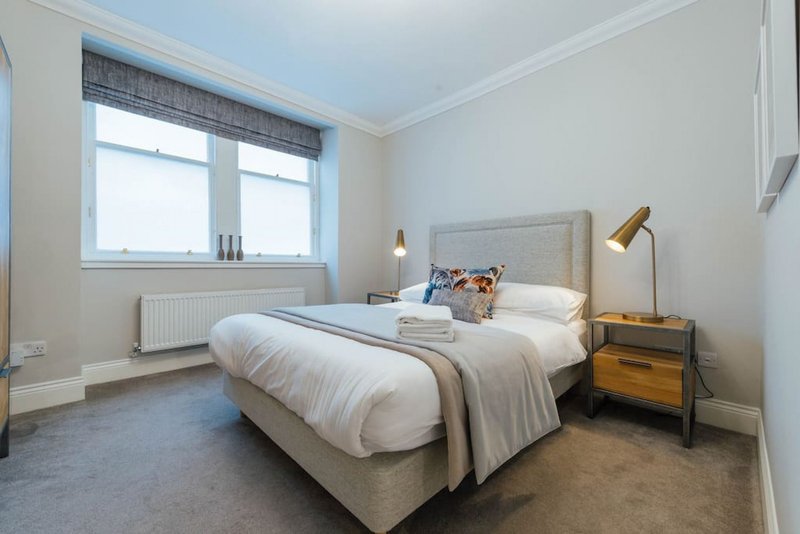 Bright bedroom with double bed, wooden nightstand, gold lamp and large window
