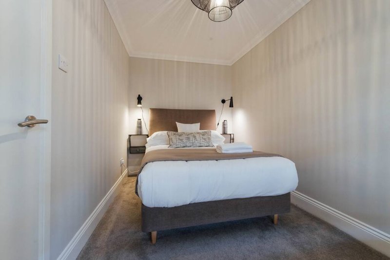 Compact bedroom with double bed, bedside lamps, striped wallpaper and wooden flooring
