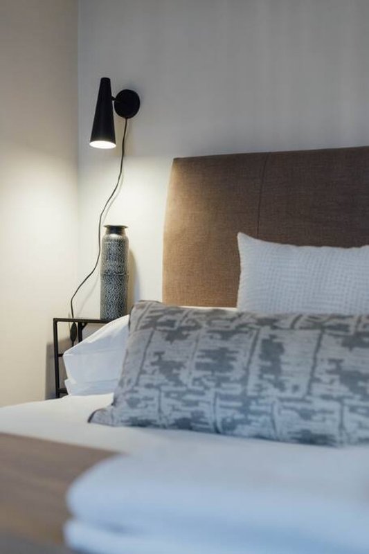 Bedroom with double bed, brown headboard, blue patterned pillows and wall-mounted black lamp