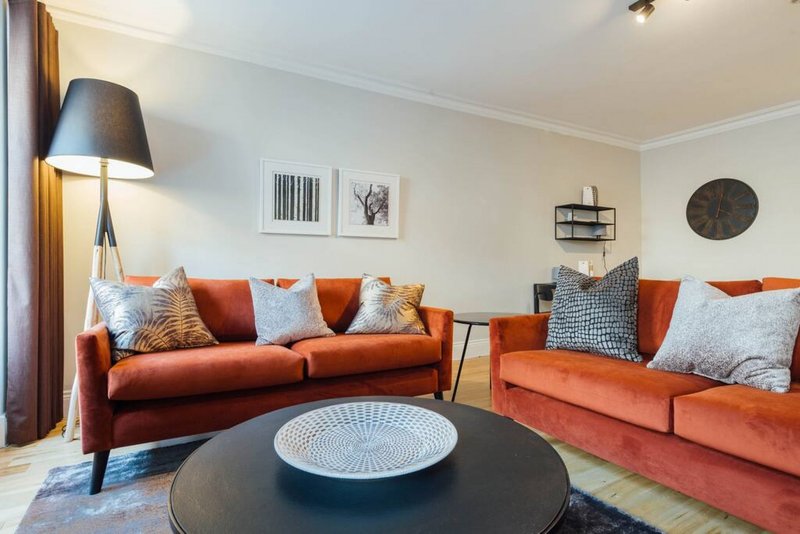 Modern living room with two orange sofas, decorative cushions, round black coffee table and wall art
