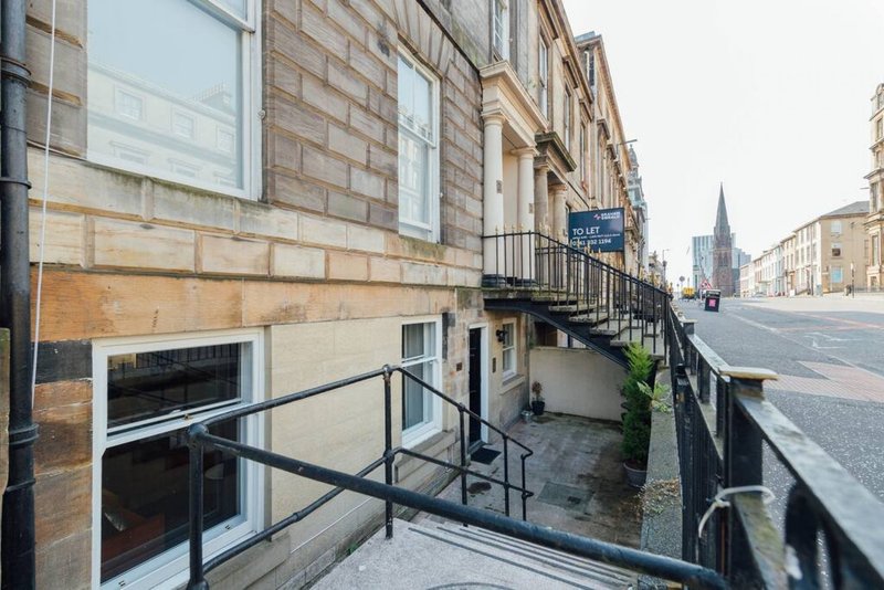 Stone townhouse exterior with street-level entrance, metal railings and steps, urban street view