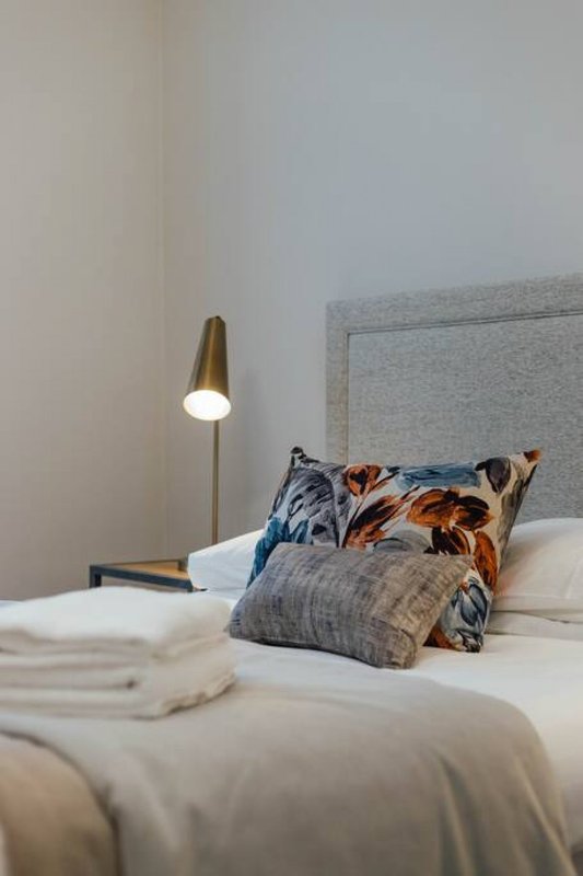 Modern bedroom with double bed, patterned pillows, brass pendant lamp and gray headboard