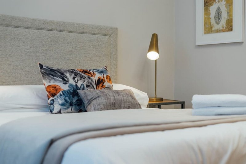 Modern bedroom with double bed, decorative pillows, bedside lamp and wall art