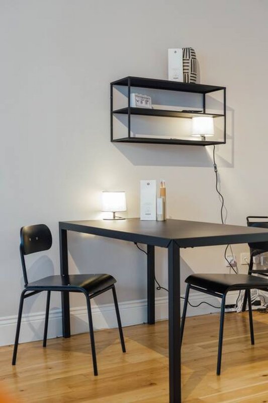 Minimalist workspace with black desk, chairs, wall-mounted shelving and desk lamp