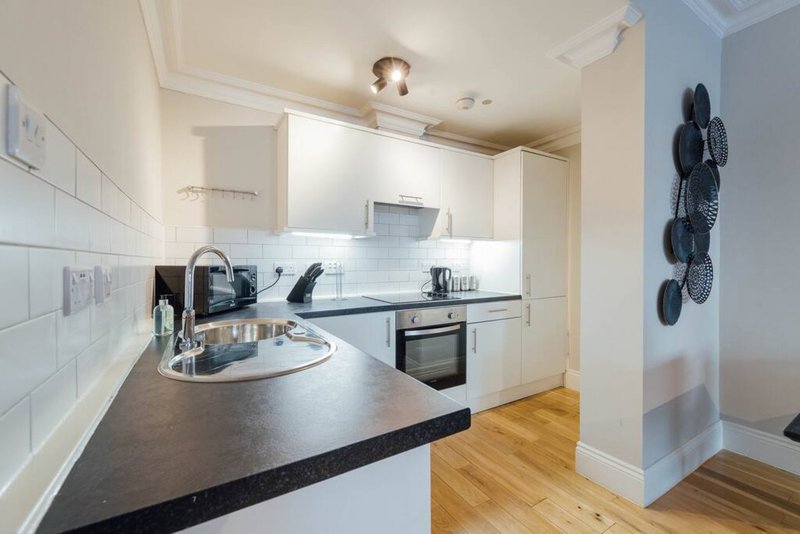 Modern kitchen with white cabinetry, black countertop, stainless steel appliances and wooden flooring