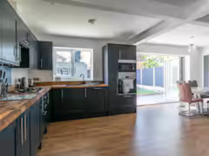Modern open-plan kitchen and living area with dark cabinetry, wooden countertops, and patio doors to garden