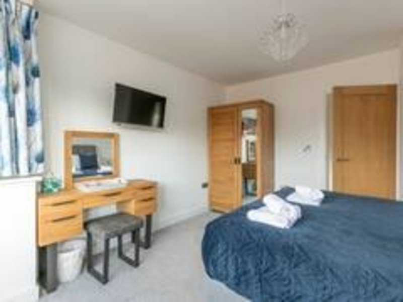 Bright bedroom with double bed, wooden dressing table, wall-mounted TV and wardrobe