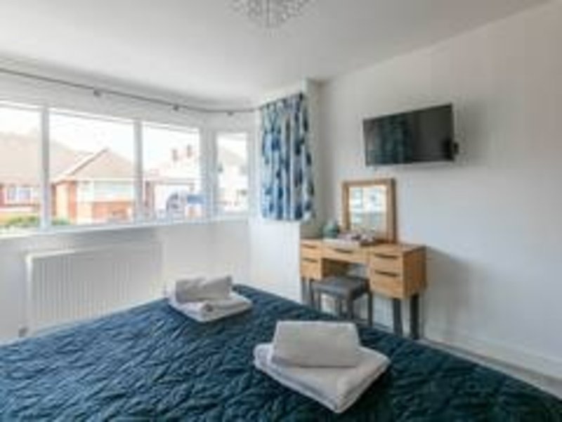 Bright bedroom with blue patterned carpet, wooden desk, wall-mounted TV and large windows