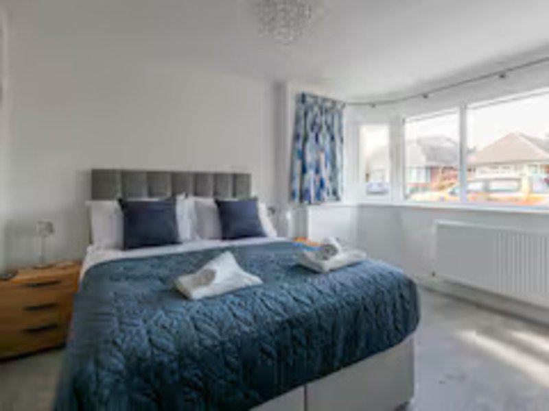 Bright bedroom with double bed, blue bedding, grey headboard and window views