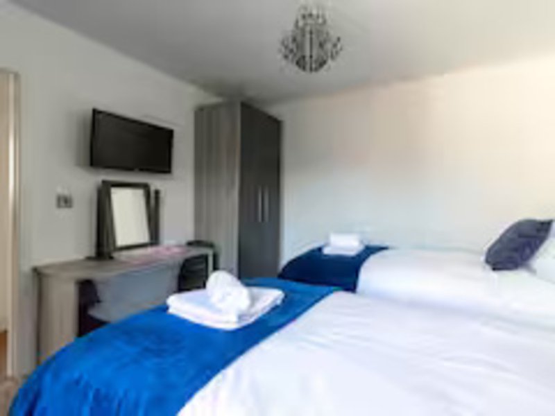 Bright bedroom with two single beds, blue bedding, wall-mounted TV, desk and wardrobe