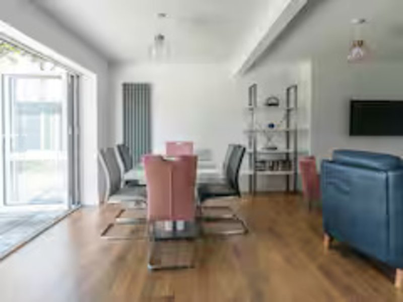 Open-plan living and dining area with wooden floor, pink dining chairs, blue sofa, and glass doors to garden