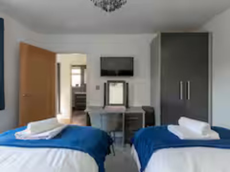 Twin bedroom with blue duvets, white pillows, desk, TV, and modern furnishings