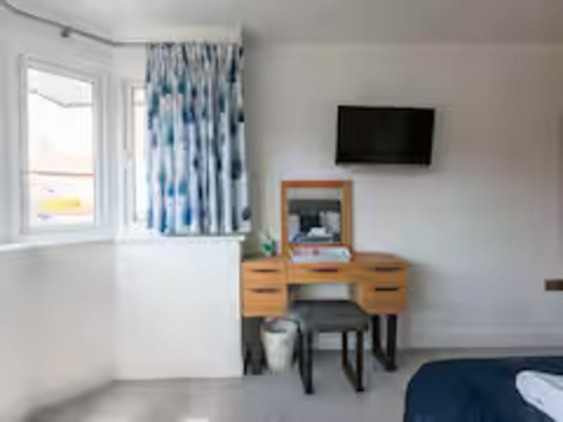 Bright bedroom with wooden desk, wall-mounted TV, blue patterned curtains and window