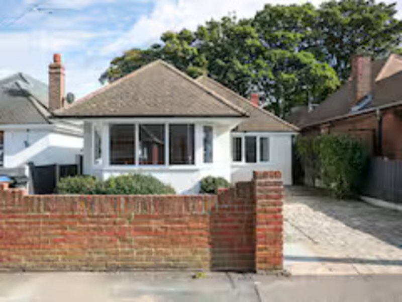 White bungalow with brick boundary wall, driveway, and mature trees