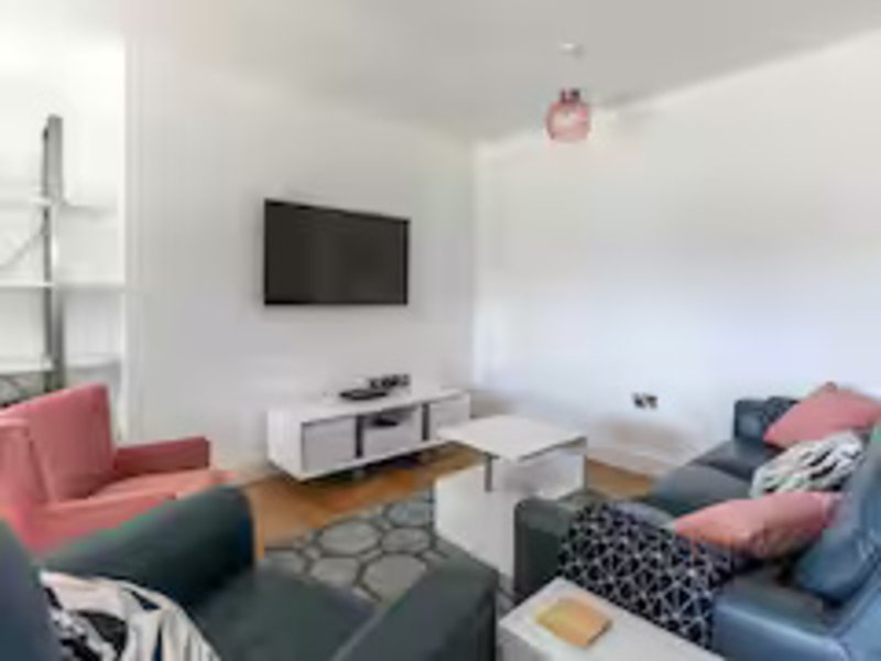 Modern living room with wall-mounted TV, gray and pink seating, wooden floor and geometric rug
