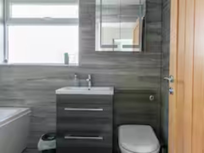 Modern bathroom with dark tile walls, white sink, mirror, toilet and window