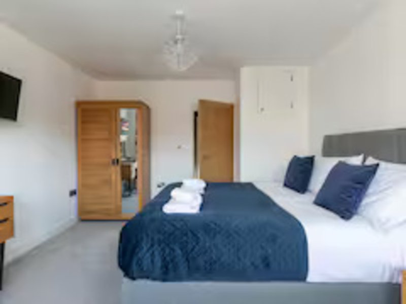 Modern bedroom with double bed, navy bedding, wooden wardrobe and white walls