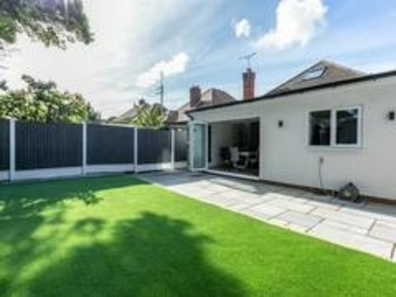 Modern single-story extension with patio, manicured lawn, and composite fencing