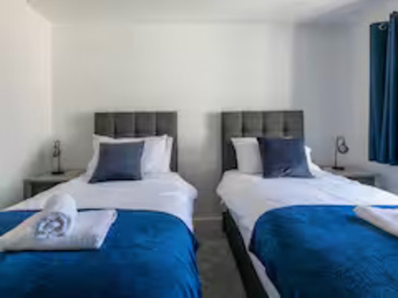 Twin bedroom with two single beds, blue bedding, grey headboards and white walls