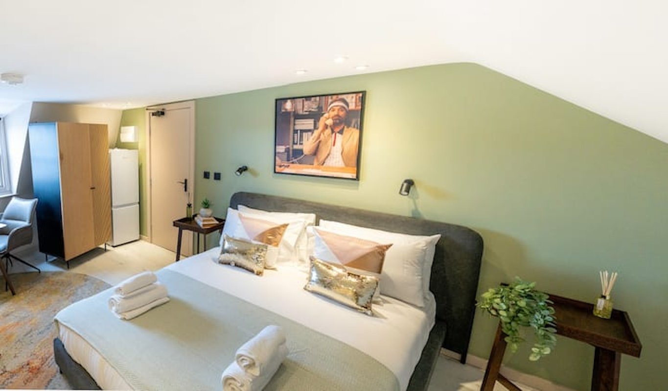 Bright bedroom with double bed, green feature wall, framed artwork and wooden furniture