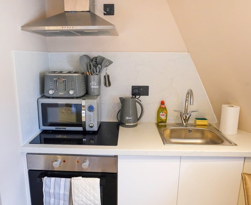 Modern kitchen corner with appliances, sink, utensils and cleaning supplies