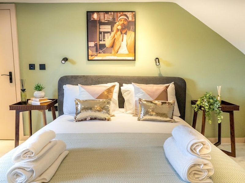 Bedroom with double bed, green walls, framed artwork, bedside tables and potted plants