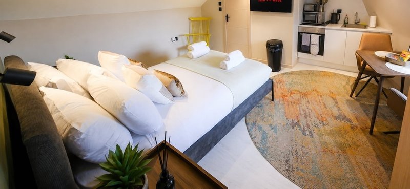 Modern bedroom with double bed, white bedding, pillows, potted plant, wooden desk and chair