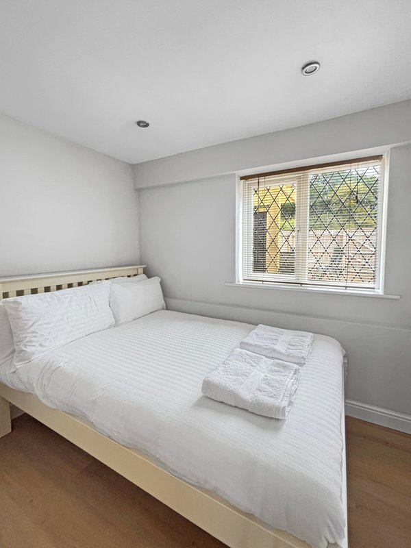 Bright bedroom with made bed, white bedding, wooden floor and leaded windows