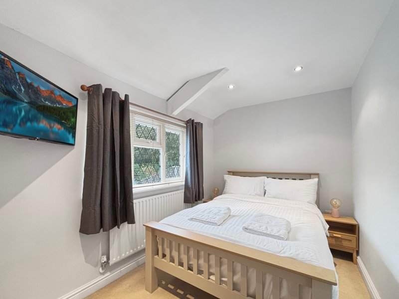 Bright bedroom with double bed, wooden nightstand, wall-mounted TV, and large window with curtains